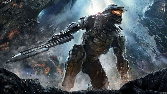 Dynamic action artwork of Master Chief from Halo standing on rocky terrain with a rifle in hand, surrounded by explosions, debris, and massive alien structures in a chaotic sci-fi battlefield.
