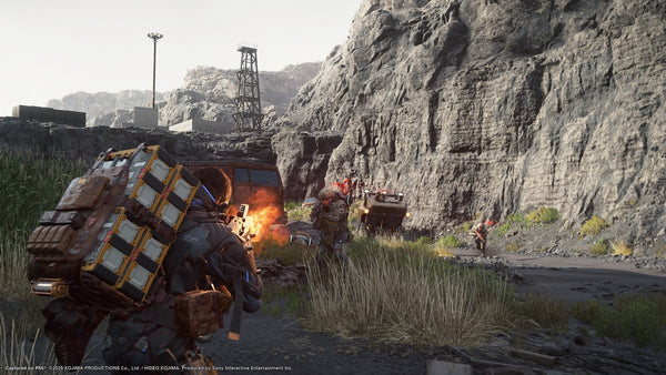 Character in a futuristic suit with a large cargo backpack fires a weapon at armed enemies on a rocky roadside, with vehicles and cliffs in the background.