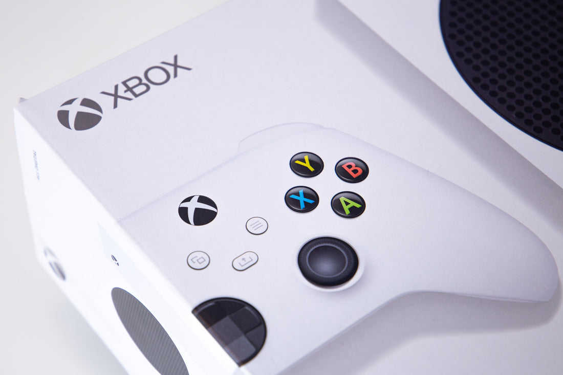 White Xbox Series S console packaging with a white Xbox wireless controller displayed on top, featuring the Xbox logo, colored ABXY buttons, and the console’s black circular vent.