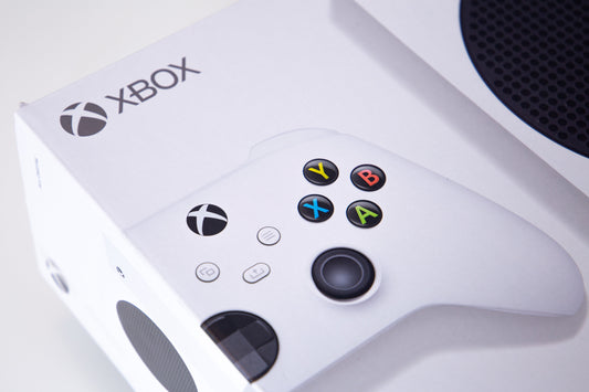White Xbox Series S console packaging with a white Xbox wireless controller displayed on top, featuring the Xbox logo, colored ABXY buttons, and the console’s black circular vent.